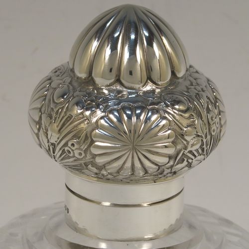 A very large and pretty pair of Antique Victorian Sterling Silver and hand-cut crystal table scent bottles, having hinged lids with gold-gilt interiors and hand-chased floral decoration, with removable internal stoppers, and hand-cut crystal main bodies. These beautiful antique silver and crystal scent bottles were made by Alfred Fuller of London in 1892. The dimensions of these fine hand-made antique silver and crystal scent bottles are height 18.5 cms (7.25 inches), width 12.5 cms (5 inches), and depth 9 cms (3.5 inches).