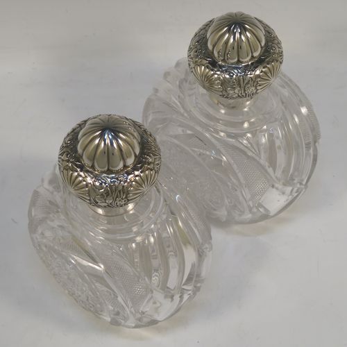 A very large and pretty pair of Antique Victorian Sterling Silver and hand-cut crystal table scent bottles, having hinged lids with gold-gilt interiors and hand-chased floral decoration, with removable internal stoppers, and hand-cut crystal main bodies. These beautiful antique silver and crystal scent bottles were made by Alfred Fuller of London in 1892. The dimensions of these fine hand-made antique silver and crystal scent bottles are height 18.5 cms (7.25 inches), width 12.5 cms (5 inches), and depth 9 cms (3.5 inches).