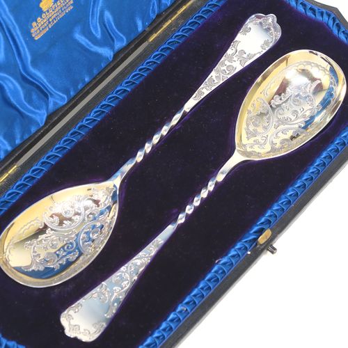 An extremely pretty pair of Antique Victorian Sterling Silver berry serving spoons, having hand-engraved handles and bowls with floral and scroll decoration, the bowls with a gold-gilt wash, and the handles with twisted middle sections, all in their original blue satin and velvet-lined presentation box. These beautiful silver serving spoons were made by the Atkin Brothers of Sheffield in 1900. The dimensions of this fine hand-made pair of antique silver berry spoons are length 21cms (8.3 inches), and they weigh a total of approx. 116g (3.7 troy ounces).  