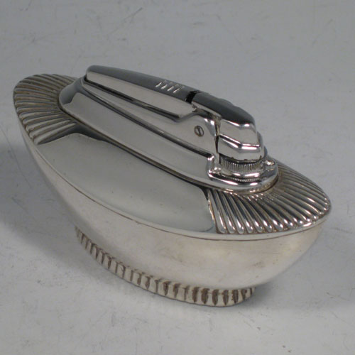    Sterling silver table lighter, having a plain oval lower body, with fluted shoulders, and sitting on a fluted collet foot. The lighter mechanism is by Ronson and is in fully working order. Length 11 cms (4.25 inches), height 6 cms (2.3 inches), width 4.5 cms (1.75 inches). Please note that this item is crested.