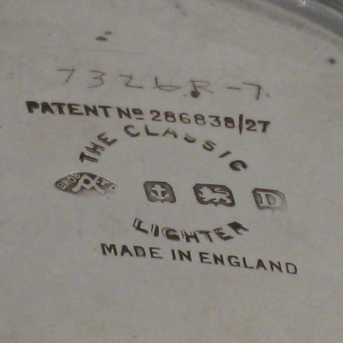 Sterling silver table lighter, having a plain cyclindrical body with engine-turned decoration, and sitting on a flat base. The lighter mechanism is patented (called The Classsic Lighter) and is in fully working order. The dimensions of this fine hand-made silver table lighter are height 9 cms (3.5 inches), diamter 5 cms (2 inches).Please note that this item is crested.   