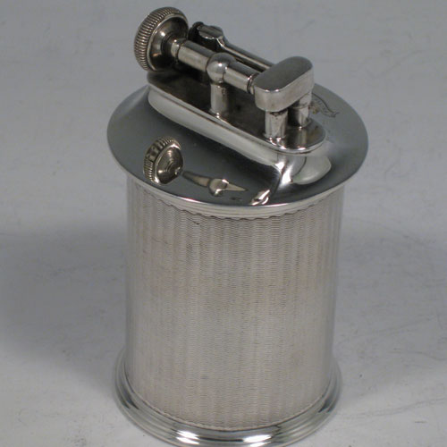 Sterling silver table lighter, having a plain cyclindrical body with engine-turned decoration, and sitting on a flat base. The lighter mechanism is patented (called The Classsic Lighter) and is in fully working order. The dimensions of this fine hand-made silver table lighter are height 9 cms (3.5 inches), diamter 5 cms (2 inches).Please note that this item is crested.   