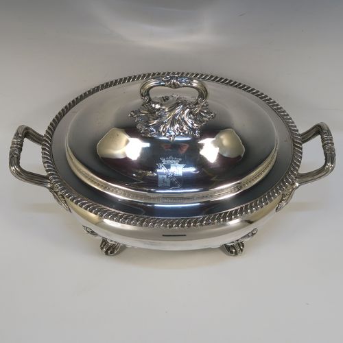 A very handsome Antique Georgian Old Sheffield Plated soup tureen in a Regency style, having an oval plain bellied body with an applied gadroon border, a domed pull-off cover with a cast anthemion leaf handle, with two cast anthemion leaf side handles, and sitting on four cast scroll  feet with floral shoulders. This elegant antique Old Sheffield Plated soup tureen and cover was made in ca. 1815. The dimensions of this fine hand-made antique Old Sheffield soup tureen are length (across handles), width 23.5 cms (9.25 inches), height 25.5 cms (10 inches). Please note that this antique Georgian Regency soup tureen is crested on the cover.   