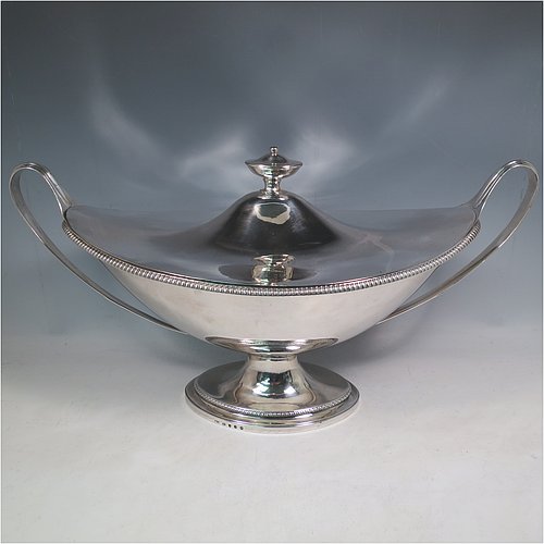 An Antique Georgian Sterling Silver large soup tureen in a boat-shape neoclassical style, having a very plain oval body with a pull-off lid and an urn-shaped finial, with applied gadroon borders, two reeded scroll side-handles, and all sitting on a pedestal foot. Made by Cornelius Bland of London in 1789. The dimensions of this fine hand-made antique silver soup tureen and cover are height 28 cms (11 inches), length including handles 52 cms (20.5 inches), width 25.5 cms (10 inches), and it weighs approx. 2,850g (92 troy ounces).    