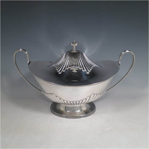 An Antique Edwardian Sterling silver soup tureen, having a pull-off lid with an urn-shaped finial and cut-out slot for a ladle, with hand-chased half-fluted decoration, applied gadroon borders, two reeded scroll side-handles, and all sitting on a pedestal foot. Made by Mappin & Webb of Sheffield in  1905. The dimensions of this fine hand-made antique silver soup tureen and cover are height 25 cms (9.75 inches), length including handles 39.5 cms (15.5 inches), width 21.5 cms (8.5 inches), and it weighs approx. 1,779 (57 troy ounces).   