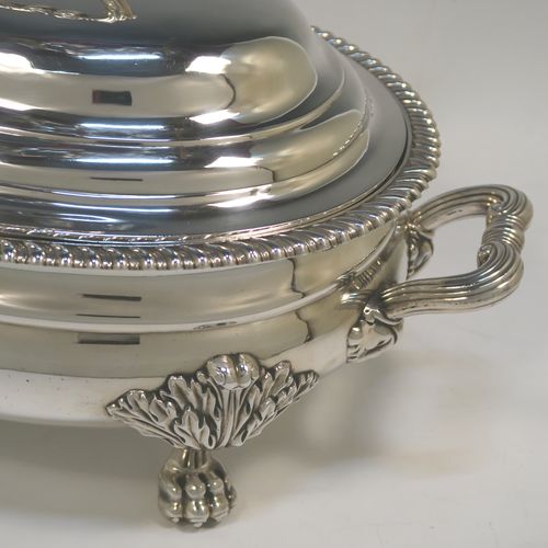 A very handsome Antique Georgian Sterling Silver Scottish soup tureen in a Regency style, having an oval plain baluster body with applied gadroon border, a domed pull-off cover with a cast anthemion leaf handle, with two cast scroll side handles, and sitting on four cast lions-paw feet with floral shoulders. This elegant antique silver soup tureen and cover was made in Edinburgh in 1815. The dimensions of this fine hand-made antique silver soup tureen are height 24 cms (9.5 inches), and width (across handles) 42 cms (16.5 inches), and it weighs approx. 3,285g (106 troy ounces). Please note that this antique Regency silver soup tureen is crested on the main body and cover.