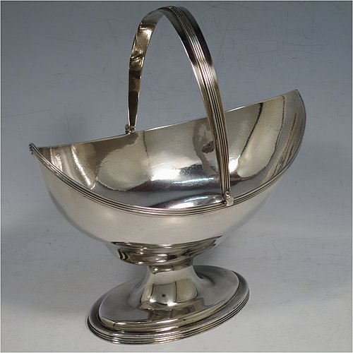 An Antique Georgian Sterling Silver sugar basket, having a plain oval bellied body, with applied reeded borders, a hinged and reeded swing-handle, and sitting on a pedestal foot.  Made by Peter & Anne Bateman of London in 1798. The dimensions of this fine hand-made antique silver sugar basket are height (inc. handle) 18 cms (7 inches), length 16.6 cms (6.5 inches), and it weighs approx. 215g (7 troy ounces).