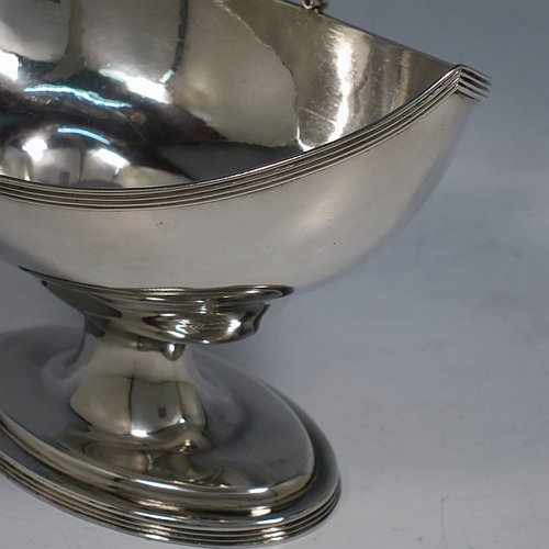 An Antique Georgian Sterling Silver sugar basket, having a plain oval bellied body, with applied reeded borders, a hinged and reeded swing-handle, and sitting on a pedestal foot.  Made by Peter & Anne Bateman of London in 1798. The dimensions of this fine hand-made antique silver sugar basket are height (inc. handle) 18 cms (7 inches), length 16.6 cms (6.5 inches), and it weighs approx. 215g (7 troy ounces).