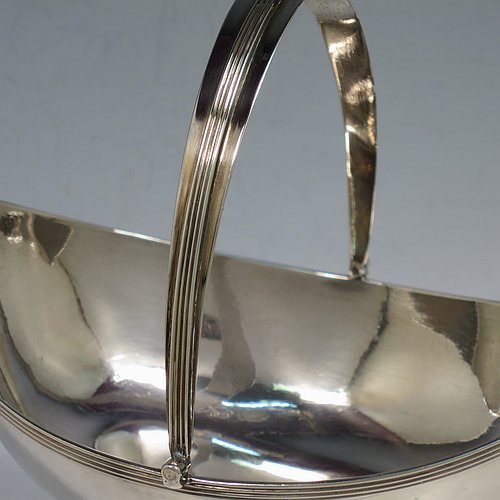 An Antique Georgian Sterling Silver sugar basket, having a plain oval bellied body, with applied reeded borders, a hinged and reeded swing-handle, and sitting on a pedestal foot.  Made by Peter & Anne Bateman of London in 1798. The dimensions of this fine hand-made antique silver sugar basket are height (inc. handle) 18 cms (7 inches), length 16.6 cms (6.5 inches), and it weighs approx. 215g (7 troy ounces).