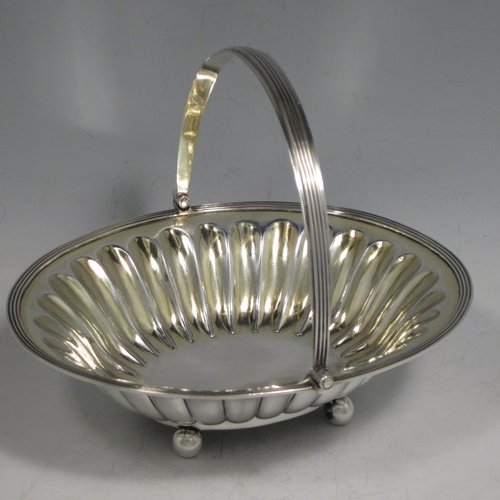 Antique Georgian sterling silver sugar or sweetmeat basket, having an oval body, with hand-chased and fluted decoration, an applied reeded border, a gold-gilt interior, a reeded swing-handle, and sitting on four ball feet. Made by William Bateman of London in 1815. The dimensions of this fine hand-made silver sugar basket are height 12.5 cms (5 inches), length 16 cms (6.25 inches), width 14 cms (5.5 inches), and it weighs approx. 174g (5.6 troy ounces).    