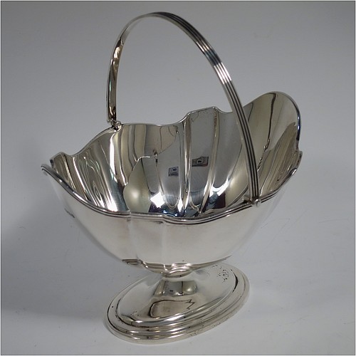 An Antique Sterling Silver sugar basket in a Georgian style, having a shaped oval body with panelled shoulders, an applied reeded border, a reeded swing-handle, and sitting on a pedestal foot. Made by Thomas Bradbury and Sons of Sheffield in 1913. The dimensions of this fine hand-made antique silver sugar basket are height 17 cms (6.75 inches), length 15 cms (6 inches), width 12.5 cms (5 inches), and it weighs approx. 231g (7.5 troy ounces).    