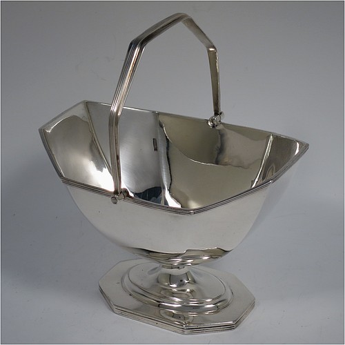 An Antique Edwardian Sterling Silver sugar basket in a Georgian style, having a plain octagonal panelled shaped body, with applied reeded borders, a reeded swing-handle, and sitting on a pedestal foot. Made by Thomas Bradbury and Sons of Sheffield in 1907. The dimensions of this fine hand-made antique silver sugar basket are height 14.5 cms (5.75 inches), length 12.5 cms (5 inches), width 10 cms (4 inches), and it weighs approx. 170g (5.5 troy ounces).    