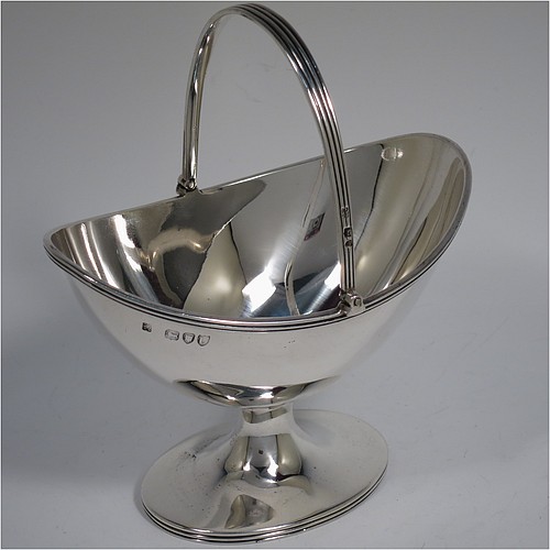 An Antique Victorian Sterling Silver sugar basket in a Georgian style, having a plain oval shaped body, with applied reeded borders, a reeded swing-handle, and sitting on a pedestal foot. Made by Holland, Aldwinckle, and Slater of London in 1895. The dimensions of this fine hand-made antique silver sugar basket are height 14.5 cms (5.75 inches), length 13 cms (5 inches), width 9.5 cms (3.75 inches), and it weighs approx. 188g (6 troy ounces).    