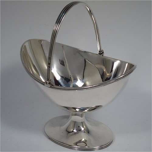 An Antique Victorian Sterling Silver sugar basket in a Georgian style, having a plain oval shaped body, with applied reeded borders, a reeded swing-handle, and sitting on a pedestal foot. Made by Holland, Aldwinckle, and Slater of London in 1895. The dimensions of this fine hand-made antique silver sugar basket are height 14.5 cms (5.75 inches), length 13 cms (5 inches), width 9.5 cms (3.75 inches), and it weighs approx. 188g (6 troy ounces).    