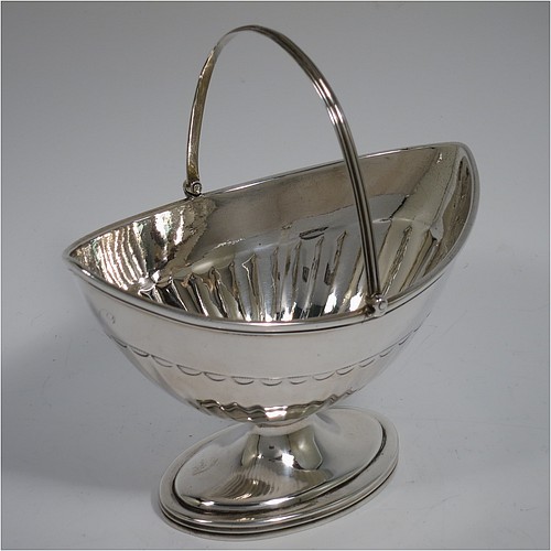 An Antique Georgian Sterling Silver sugar basket, having an oval bellied body with hand-chased half-fluting, with applied reeded borders, a hinged and reeded swing-handle, and sitting on a pedestal foot. Made by Peter & Anne Bateman of London in 1791. The dimensions of this fine hand-made antique silver sugar basket are height (inc. handle) 15 cms (6 inches), length 14 cms (5.5 inches), and it weighs approx. 198g (6.4 troy ounces).   