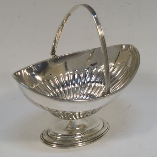 A very pretty Antique Victorian Sterling Silver sugar basket, having an oval body with tapering sides and hand-chased half-fluted decoration, with an applied reeded top border, a hinged and reeded swing-handle, and sitting on a plain oval stepped pedestal foot. This beautiful antique silver sweet-meat basket was made by Thomas Bradbury of London in 1897. The dimensions of this fine hand-made antique silver sugar basket are height (inc. handle) 13.5 cms (5.3 inches), length 13.5 cms (5.3 inches), width 9.5 cms (3.75 inches), and it weighs approx. 132g (4.3 troy ounces).   