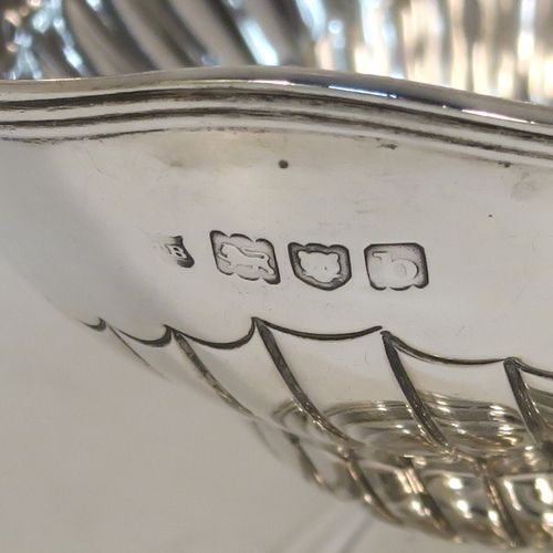 A very pretty Antique Victorian Sterling Silver sugar basket, having an oval body with tapering sides and hand-chased half-fluted decoration, with an applied reeded top border, a hinged and reeded swing-handle, and sitting on a plain oval stepped pedestal foot. This beautiful antique silver sweet-meat basket was made by Thomas Bradbury of London in 1897. The dimensions of this fine hand-made antique silver sugar basket are height (inc. handle) 13.5 cms (5.3 inches), length 13.5 cms (5.3 inches), width 9.5 cms (3.75 inches), and it weighs approx. 132g (4.3 troy ounces).   