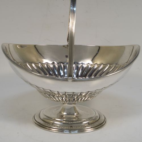 A very pretty Antique Victorian Sterling Silver sugar basket, having an oval body with tapering sides and hand-chased half-fluted decoration, with an applied reeded top border, a hinged and reeded swing-handle, and sitting on a plain oval stepped pedestal foot. This beautiful antique silver sweet-meat basket was made by Thomas Bradbury of London in 1897. The dimensions of this fine hand-made antique silver sugar basket are height (inc. handle) 13.5 cms (5.3 inches), length 13.5 cms (5.3 inches), width 9.5 cms (3.75 inches), and it weighs approx. 132g (4.3 troy ounces).   