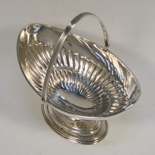 A very pretty Antique Victorian Sterling Silver sugar basket, having an oval body with tapering sides and hand-chased half-fluted decoration, with an applied reeded top border, a hinged and reeded swing-handle, and sitting on a plain oval stepped pedestal foot. This beautiful antique silver sweet-meat basket was made by Thomas Bradbury of London in 1897. The dimensions of this fine hand-made antique silver sugar basket are height (inc. handle) 13.5 cms (5.3 inches), length 13.5 cms (5.3 inches), width 9.5 cms (3.75 inches), and it weighs approx. 132g (4.3 troy ounces).   