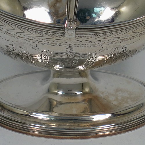 A very pretty Antique Georgian Sterling Silver sugar basket, having an oval bellied body in a Neoclassical style with hand-engraved floral and swag decoration, applied reeded borders, a hinged and reeded swing-handle, and sitting on a pedestal foot. Made by Henry Chawner of London in 1790. The dimensions of this fine hand-made antique silver sugar basket are height (inc. handle) 12.5 cms (5 inches), length 12.5 cms (5 inches), and it weighs approx. 151g (4.9 troy ounces).   