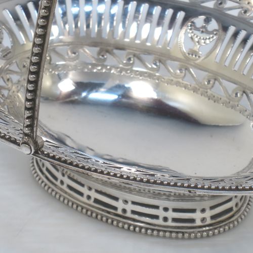 A very pretty Antique Georgian Sterling Silver sugar or sweetmeat basket, having an oval body, with hand-pierced neoclassical style decoration, an applied bead-edged border, a beeded swing-handle, and sitting on a matching pedestal foot. Made by Robert Hennell of London in 1781. The dimensions of this fine hand-made antique silver sweet-meat or sugar basket are height 13 cms (5 inches), length 15.5 cms (6 inches), width 12.5 cms (5 inches), and it weighs approx. 156g (5 troy ounces).  