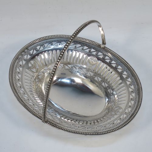 A very pretty Antique Georgian Sterling Silver sugar or sweetmeat basket, having an oval body, with hand-pierced neoclassical style decoration, an applied bead-edged border, a beeded swing-handle, and sitting on a matching pedestal foot. Made by Robert Hennell of London in 1781. The dimensions of this fine hand-made antique silver sweet-meat or sugar basket are height 13 cms (5 inches), length 15.5 cms (6 inches), width 12.5 cms (5 inches), and it weighs approx. 156g (5 troy ounces).  