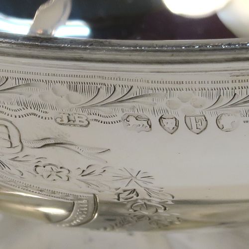 A very pretty Antique Victorian Sterling Silver sugar basket, having an oval body with tapering sides and hand-engraved bright-cut floral style decoration above two cartouches on either side, with applied reeded borders, a hinged and reeded swing-handle, and sitting on a plain oval pedestal foot. This beautiful antique silver sweet-meat basket was made by Joseph Braham of London in 1881. The dimensions of this fine hand-made antique silver sugar basket are height (inc. handle) 15 cms (6 inches), length 16 cms (6.3 inches), width 10 cms (4 inches), and it weighs approx. 178g (5.7 troy ounces). Please note that this item has a part-crest on one side.