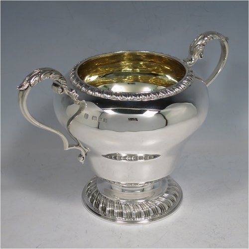 A Sterling Silver large sugar bowl, in a Georgian style, having a plain round baluster body, with an applied gadroon border, two scroll side-handles with Anthemion leaf thumb-pieces, a gold-gilt interior, and all sitting on a pedestal foot with hand-chased fluted decoration. Made by Charles Townley & John Thomas of London in 1928. The dimensions of this fine hand-made silver sugar bowl are height 13.5 cms (5.25 inches), spread across handles 19 cms (7.5 inches), and it weighs approx. 448g (14.5 troy ounces).   