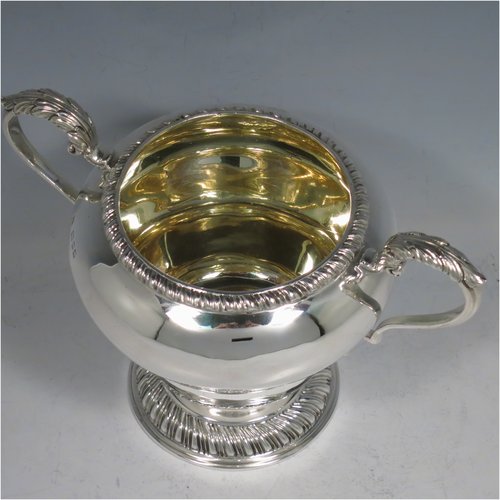 A Sterling Silver large sugar bowl, in a Georgian style, having a plain round baluster body, with an applied gadroon border, two scroll side-handles with Anthemion leaf thumb-pieces, a gold-gilt interior, and all sitting on a pedestal foot with hand-chased fluted decoration. Made by Charles Townley & John Thomas of London in 1928. The dimensions of this fine hand-made silver sugar bowl are height 13.5 cms (5.25 inches), spread across handles 19 cms (7.5 inches), and it weighs approx. 448g (14.5 troy ounces).   