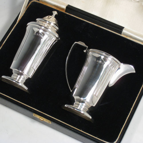 Sterling silver pair of Art Deco sugar caster and creamer set, having plain round bodies with tapering sides and reeded hand-chased decoration, a pull-off hand-pierced lid on the caster and a loop handle on the creamer, all sitting on round pedestal feet, and in their original satin and velvet-lined presentation box. Made in Birmingham in 1938. The dimensions of this fine hand-made silver sugar caster and cream jug set are height of caster 14 cms (5.5 inches), length of cream jug (11 cms (4.3 inches), and the total weight is approx. 217g (7 troy ounces).  