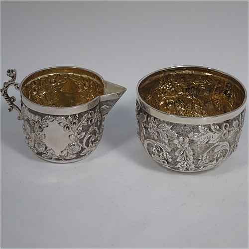 A beautiful Antique Victorian Sterling Silver sugar and creamer set, having round bodies with hand-chased floral decoration, and with gold-gilt interiors, all sitting on flat bases. Made by James Wakely & Frank Clarke Wheeler of London in 1890. The dimensions of this fine hand-made antique silver sugar and creamer set are diameter of sugar bowl 8 cms (3 inches), height of cream jug 6.5 cms (2.5 inches), and with a total weight of 133g (4.3 troy ounces).    