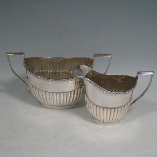 Antique Edwardian sterling silver sugar and creamer set, having oval bodies with hand-chased half-fluted decoration, applied gadroon borders, and reeded handles. Made by William Aitken of Birmingham in 1902. Height 10 cms (4 inches), length of sugar bowl 19 cms (7.5 inches). Total weight approx. 419g (13.5 troy ounces).