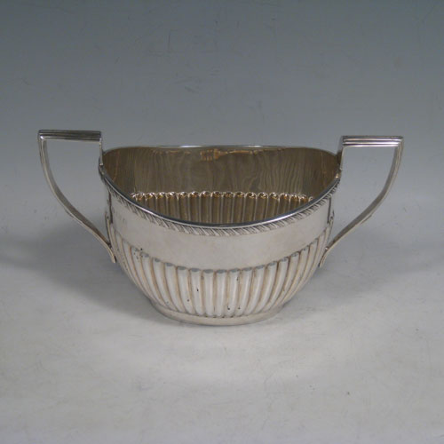 Antique Edwardian sterling silver sugar and creamer set, having oval bodies with hand-chased half-fluted decoration, applied gadroon borders, and reeded handles. Made by William Aitken of Birmingham in 1902. Height 10 cms (4 inches), length of sugar bowl 19 cms (7.5 inches). Total weight approx. 419g (13.5 troy ounces).