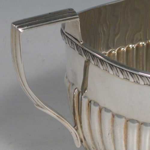 Antique Edwardian sterling silver sugar and creamer set, having oval bodies with hand-chased half-fluted decoration, applied gadroon borders, and reeded handles. Made by William Aitken of Birmingham in 1902. Height 10 cms (4 inches), length of sugar bowl 19 cms (7.5 inches). Total weight approx. 419g (13.5 troy ounces).