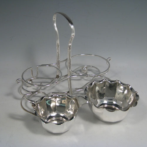 Sterling silver sugar and cream set in a frame, having round panelled bodies with scroll edges, and flat bases, all sitting in an original wire-work frame on four ball feet. Made by James Dixon and Sons of Sheffield in 1913. Height 18 cms (7 inches), length 22 cms (8.5 inches), width 12.5 cms (5 inches). Total weight 495g (16 troy ounces)