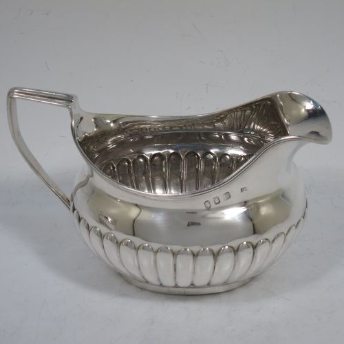 A very handsome Antique Georgian Irish Sterling Silver sugar bowl and cream jug set, having oval bellied bodies with hand-chased half-fluted decoration, applied reeded borders and flat-topped side-handles, and all sitting on collet feet. Made by James Scott of Dublin in 1806. The dimensions of this fine hand-made antique Irish silver sugar and creamer set are length of sugar bowl (inc. handles) 20 cms (8 inches), height 10 cms (4 inches), width 13 cms (5 inches), with a total weight of approx. 436g (14 troy ounces).    