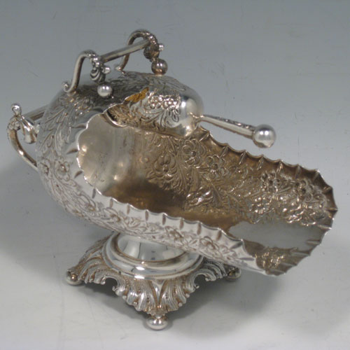 Antique Victorian sterling silver sugar scuttle, having a hand-chased body with floral decoration, two cast twin-scroll handles, an original scoop with gold-gilt interior, and sitting on a pedestal foot with four cushion feet. Made by Walker and Hall of Birmingham in 1899. Length 16 cms (6.25 inches), height 12.5 cms (5 inches), width 8 cms (3 inches). Weight approx. 216g (7 troy ounces).