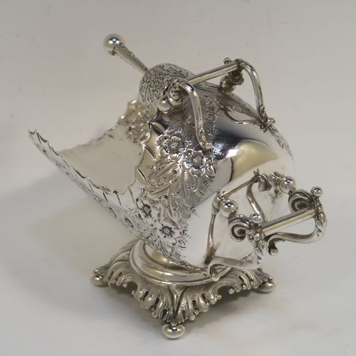 A rare and very pretty Antique Victorian Sterling Silver sugar scuttle, having a hand-chased body with floral decoration, two cast twin-scroll handles, an original scoop, and sitting on a pedestal foot with four cushion feet. This beautiful antique silver sugar scuttle was made by William Davenport of Birmingham in 1900. The dimensions of this fine hand-made silver sugar scuttle are length 15 cms (6 inches), height 12 cms (4.75 inches), width 8 cms (3 inches), and it weighs approx. 209g (6.7 troy ounces).   