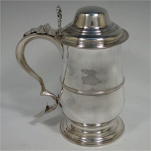 A very handsome Antique Georgian Sterling Silver lidded quart tankard, having a plain round bellied body with central reeded girdle, a hinged dome lid with hand-pierced thumb-piece, a scroll handle with heart-shaped terminal, and sitting on a pedestal foot. Made by Peter and Anne Bateman of London in 1795. The dimensions of this fine hand-made antique silver quart tankard are height 21 cms (8.25 inches), length 18 cms (7 inches), and it weighs approx. 767g (24.7 troy ounces).   