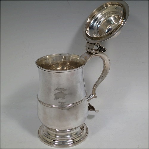 A very handsome Antique Georgian Sterling Silver lidded quart tankard, having a plain round bellied body with central reeded girdle, a hinged dome lid with hand-pierced thumb-piece, a scroll handle with heart-shaped terminal, and sitting on a pedestal foot. Made by Peter and Anne Bateman of London in 1795. The dimensions of this fine hand-made antique silver quart tankard are height 21 cms (8.25 inches), length 18 cms (7 inches), and it weighs approx. 767g (24.7 troy ounces).   