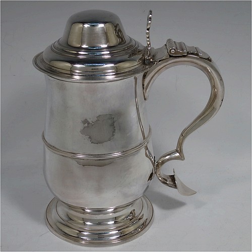 A very handsome Antique Georgian Sterling Silver lidded quart tankard, having a plain round bellied body with central reeded girdle, a hinged dome lid with hand-pierced thumb-piece, a scroll handle with heart-shaped terminal, and sitting on a pedestal foot. Made by Peter and Anne Bateman of London in 1795. The dimensions of this fine hand-made antique silver quart tankard are height 21 cms (8.25 inches), length 18 cms (7 inches), and it weighs approx. 767g (24.7 troy ounces).   