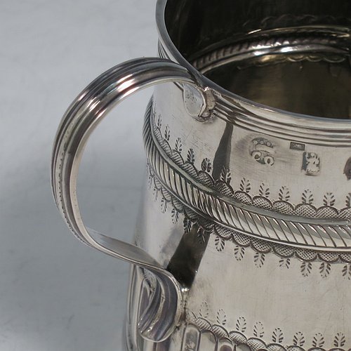 An Antique Queen Anne Sterling Silver half-pint mug / tankard, having a round straight-sided body, with reeded borders, hand-chased fluted and gadroon decoration, a scroll reeded handle, a vacant oval cartouche with scroll-work surround, and sitting on a collet foot. Made by John Cory of London in 1702. The dimensions of this fine hand-made antique silver tankard / mug are height 9 cms (3.5 inches), diameter at top 6.5 cms (2.5 inches), and it weighs approx. 116g (3.7 troy ounces).   