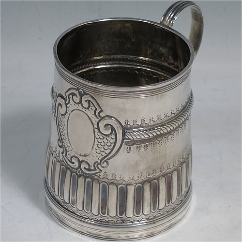 An Antique Queen Anne Sterling Silver half-pint mug / tankard, having a round straight-sided body, with reeded borders, hand-chased fluted and gadroon decoration, a scroll reeded handle, a vacant oval cartouche with scroll-work surround, and sitting on a collet foot. Made by John Cory of London in 1702. The dimensions of this fine hand-made antique silver tankard / mug are height 9 cms (3.5 inches), diameter at top 6.5 cms (2.5 inches), and it weighs approx. 116g (3.7 troy ounces).   