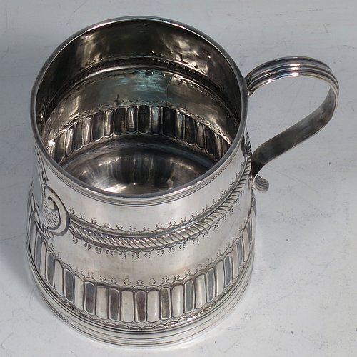 An Antique Queen Anne Sterling Silver half-pint mug / tankard, having a round straight-sided body, with reeded borders, hand-chased fluted and gadroon decoration, a scroll reeded handle, a vacant oval cartouche with scroll-work surround, and sitting on a collet foot. Made by John Cory of London in 1702. The dimensions of this fine hand-made antique silver tankard / mug are height 9 cms (3.5 inches), diameter at top 6.5 cms (2.5 inches), and it weighs approx. 116g (3.7 troy ounces).   