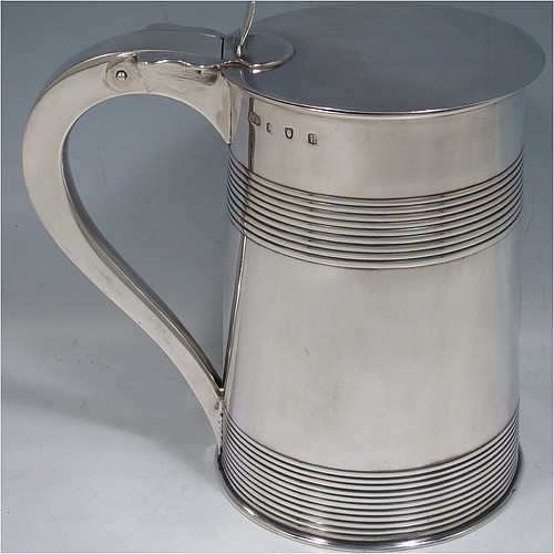 An Antique Georgian Sterling Silver lidded quart tankard, having a plain round straight-sided body with two bands of hand-chased reeded decoration, gold-gilt interior, a hinged flat lid with thumb-piece, a scroll handle, and sitting on a flat base. Made by Edward Fernell  of London in 1783. The dimensions of this fine hand-made antique silver tankard are height 16.5 cms (6.5 inches), length 17 cms (6.75 inches), and it weighs approx. 757g (24.4 troy ounces). Please note that this item is crested.   