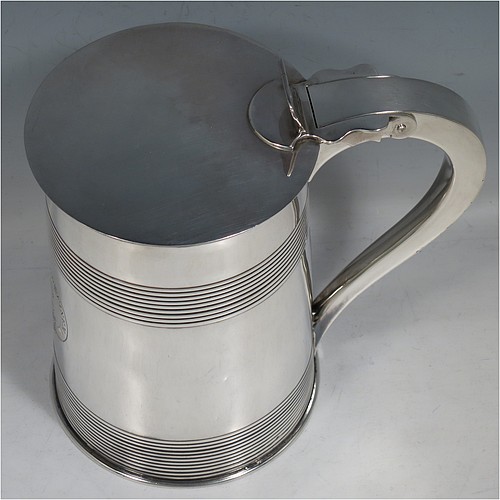 An Antique Georgian Sterling Silver lidded quart tankard, having a plain round straight-sided body with two bands of hand-chased reeded decoration, gold-gilt interior, a hinged flat lid with thumb-piece, a scroll handle, and sitting on a flat base. Made by Edward Fernell  of London in 1783. The dimensions of this fine hand-made antique silver tankard are height 16.5 cms (6.5 inches), length 17 cms (6.75 inches), and it weighs approx. 757g (24.4 troy ounces). Please note that this item is crested.   