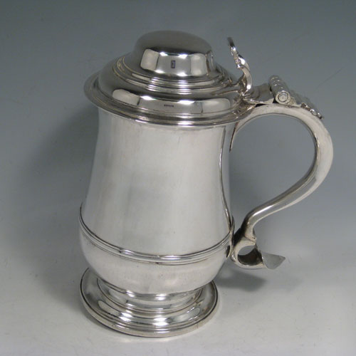 Antique Georgian sterling silver lidded quart tankard, having a plain bellied body, a hinged dome lid with thumb-piece, a scroll handle, sitting on a pedestal foot. Made by William Cripps of London in 1760. Weight approx. 758g (24.5 troy ounces). Please note that this piece has a small part-crest on the front of the body.