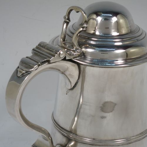 A very handsome Antique Georgian Sterling Silver lidded quart tankard, having a plain round bellied body with central reeded girdle, a hinged dome lid with hand-pierced thumb-piece, a scroll handle with heart-shaped terminal, and sitting on a pedestal foot. Made by James Young (overstriking another) of London in 1782. The dimensions of this fine hand-made antique silver quart tankard are height 19.5 cms (7.75 inches), length 17 cms (6.75 inches), and it weighs approx. 745g (24 troy ounces).    