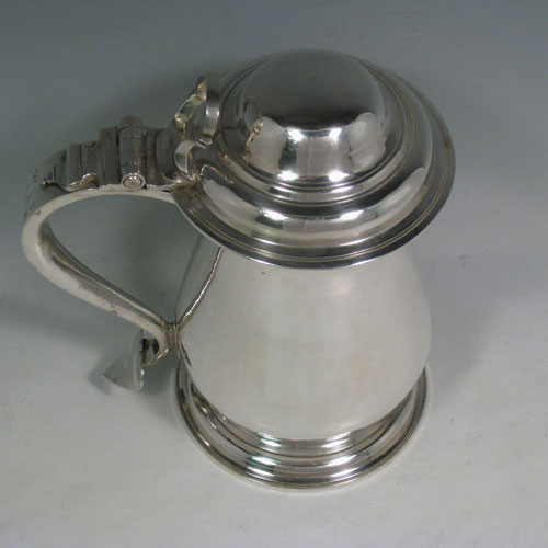 An Antique Georgian Sterling Silver lidded quart tankard, having a plain round bellied body, a hinged dome lid with thumb-piece, a scroll handle with heart-shaped terminal, sitting on a pedestal foot. Made by Whipham and Wright of London in 1760. The dimensions of this fine hand-made antique silver tankard are height 19 cms (7.5 inches), length 16 cms (6.25 inches), and it weighs approx. 723g (23 troy ounces).