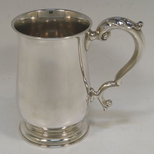 A very handsome Sterling Silver pint tankard or mug, having a plain round bellied body, a scroll handle with anthemion leaf thumb-piece, and sitting on a pedestal foot. This elegant sterling silver pint mug was made by Goldsmiths and Silversmiths of London in 1938. The dimensions of this fine hand-made silver pint tankard are height 14 cms (5.5 inches), diameter at top 8.5 cms (3.3 inches), and it weighs approx. 295g (9.5 troy ounces). Please note that the inside is finished off in a Butler finish which is not as bright as the outside.   